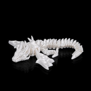 May include: A white, 3D-printed dragon figurine. The dragon is lying down, with detailed scales, claws, and a textured head. The figurine is set against a black background, highlighting its intricate design.