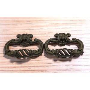 May include: Two antique bronze-colored drawer pulls. Each pull features an ornate floral design at the top and a twisted rope-like handle. The pulls are likely made of metal and are designed for furniture.