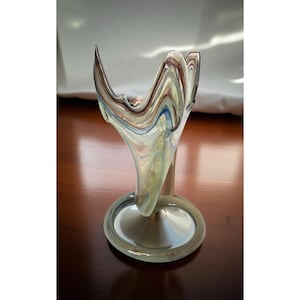 May include: A decorative glass vase with a unique, organic shape. The vase features a flared top with swirling patterns of blue, brown, and white. It sits on a round, clear base. The vase is approximately 8 inches tall.