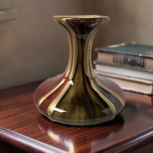Può includere: Un vaso in ceramica con base ampia e arrotondata e collo svasato, caratterizzato da una finitura lucida con pannelli alternati di rosso intenso, verde oliva scuro e nero, separati da sottili linee verticali di colore dorato.