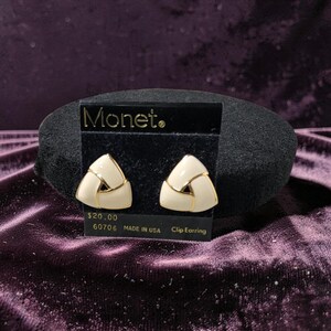 May include: Cream-colored Monet clip earrings with gold-tone accents, triangular design. The earrings are displayed on a black card with the Monet logo and the text "Clip Earring".