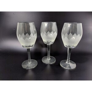 May include: Three clear wine glasses with a frosted floral design on the bowl. The glasses have a slender stem and a round base. The background is a solid black.