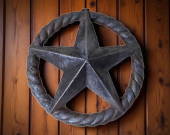May include: A rustic, dark metal star-shaped wall hanging with a rope-like border. The star is centered within the circular border and is mounted on a wooden door. The star is approximately 12 inches in diameter.
