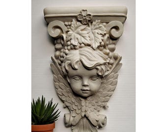 May include: A detailed, off-white wall sculpture featuring a cherub's face with grapes, leaves, and wings. The sculpture is mounted on a decorative architectural element. A potted succulent plant sits below the sculpture.