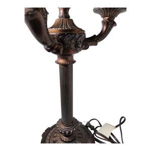 May include: A dark bronze-toned metal candelabra lamp featuring a fluted central column, an ornate circular base with leaf-like detailing, and two curved arms extending upward to support candle-style light sockets with scalloped edges.