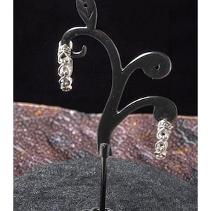 May include: Silver hoop earrings with a detailed heart and ornate design. The earrings are displayed on a black jewellery stand, highlighting their intricate craftsmanship and elegant style. A classic accessory.