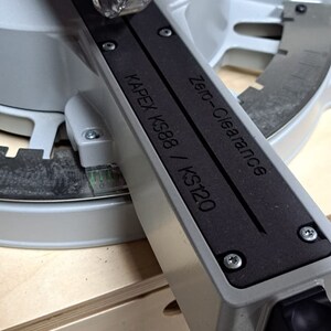 May include: A close-up of a gray and black saw blade guard with the text "Zero-Clearance" and "KAPEX KS88 / KS120" printed on it.
