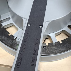 May include: A gray and black zero-clearance insert for a Kapex KS88 / KS120 saw. The insert has a black rubber strip and is being secured with a screw.