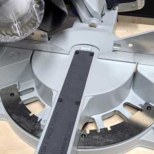 May include: A gray and black miter saw with a black handle and a green lever. The saw is labeled "Zero-Clearance" and "KAPEKS KS383 / KS120".