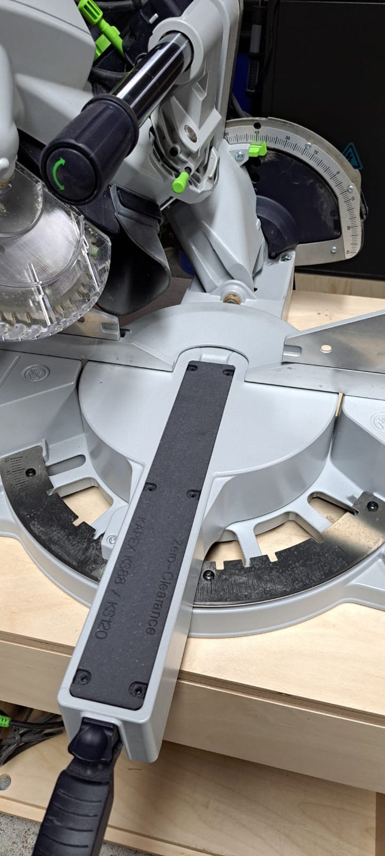 May include: A gray and black miter saw with a black handle and a green lever. The saw is labeled "Zero-Clearance" and "KAPEKS KS383 / KS120".
