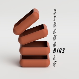 Può includere: Quattro contenitori impilabili rettangolari color terracotta sono disposti in una torre inclinata. Il testo "STACKABLE BINS" è allineato verticalmente sul lato destro dell'immagine. I contenitori hanno angoli arrotondati e una finitura liscia.