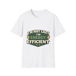Puede incluir: Camiseta blanca con el texto "I'M NOT LAZY I'M ENERGY EFFICIENT" en un diseño verde, amarillo y negro. El gráfico tiene forma de escudo con rayos y estrellas.