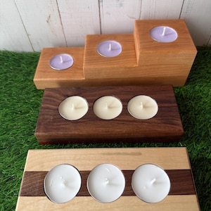 Puede incluir: Candelabros de madera en varios diseños. Uno es un diseño escalonado con tres velas lavanda. Dos soportes rectangulares con tres velas blancas cada uno. Un soporte es de madera oscura, el otro es de madera clara con una franja de madera oscura.
