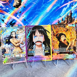 K&ouml;nnte beinhalten: Drei One Piece Sammelkarten mit Nico Robin in verschiedenen k&uuml;nstlerischen Stilen. Die Karten zeigen Charakterillustrationen, Text und Spielstatistiken, einschlie&szlig;lich St&auml;rkewerten von 5000, vor einem lebendigen, farbenfrohen Hintergrund.