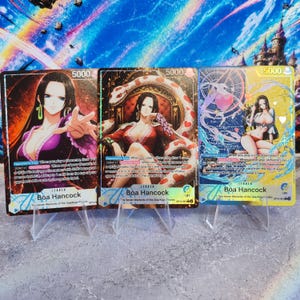May include: Three One Piece trading cards featuring Boa Hancock as the leader. Each card displays the character in different poses with a power level of 5000, text detailing game abilities, and the name Boa Hancock printed at the bottom.