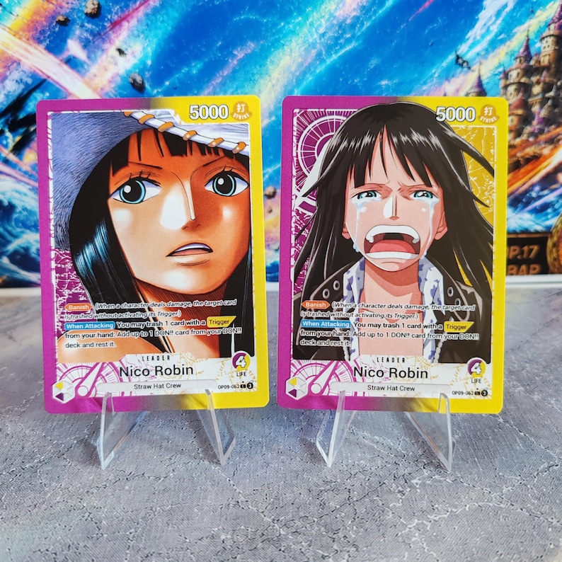 K&ouml;nnte beinhalten: Zwei One Piece Sammelkarten mit Nico Robin als Anf&uuml;hrerin. Die linke Karte zeigt eine Nahaufnahme von Nico Robin mit Hut, w&auml;hrend die rechte Karte sie weinend darstellt. Beide Karten haben eine St&auml;rke von 5000, 4 Leben und den Text Straw Hat Crew.
