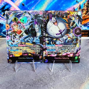 May include: Two One Piece trading cards featuring Gecko Moria as a leader. The left card shows Perona and Moria with 5000 power. The right card depicts a large, pale, horned Moria with a purple anchor weapon. Both cards display game text and stats.