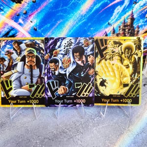 Op de afbeelding: Drie rechthoekige ruilkaarten met anime-stijl illustraties van personages in militaire uniformen. Elke kaart toont de tekst "Your Turn +1000" onderaan, "DON!! CARD" in kleine letters en Japanse tekens op de middelste kaart.