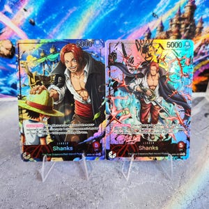 May include: Two One Piece trading cards featuring the character Shanks. The left card shows Shanks with a straw hat-wearing figure, while the right card depicts Shanks in a dynamic pose with a sword. Both cards display 5000 power and 5 life.