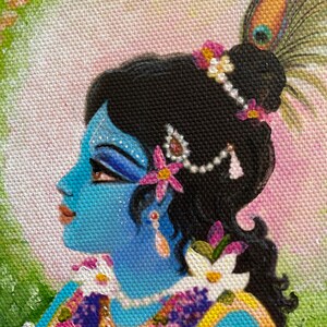May include: A side profile of a painting of a blue-skinned figure adorned with floral and jeweled embellishments. The figure has black hair, a peacock feather, and wears a necklace with pink roses. The background is a mix of pink and green.