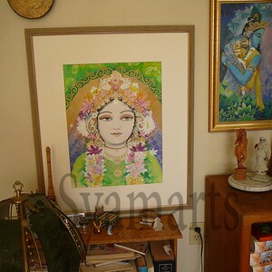 May include: A framed painting of a woman with a flower crown and a green background. The painting is in a gold frame and is hanging on a wall. There is a smaller framed painting of a couple in the background.
