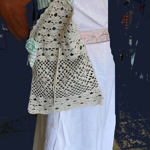 May include: A white crocheted bag with a green and white striped strap. The bag has a floral embellishment and a drawstring closure.