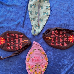 May include: An assortment of handmade fabric pouches in various colors and designs. One pouch is light blue with a repeating elephant pattern, another is lavender with floral embroidery and the text "Shri Radha". Two are brown with embroidered text and a lotus flower.