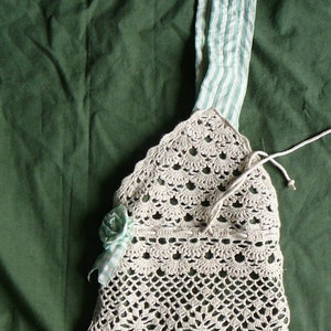 May include: A crocheted beige bag with a green and white striped fabric strap and a crocheted flower embellishment.