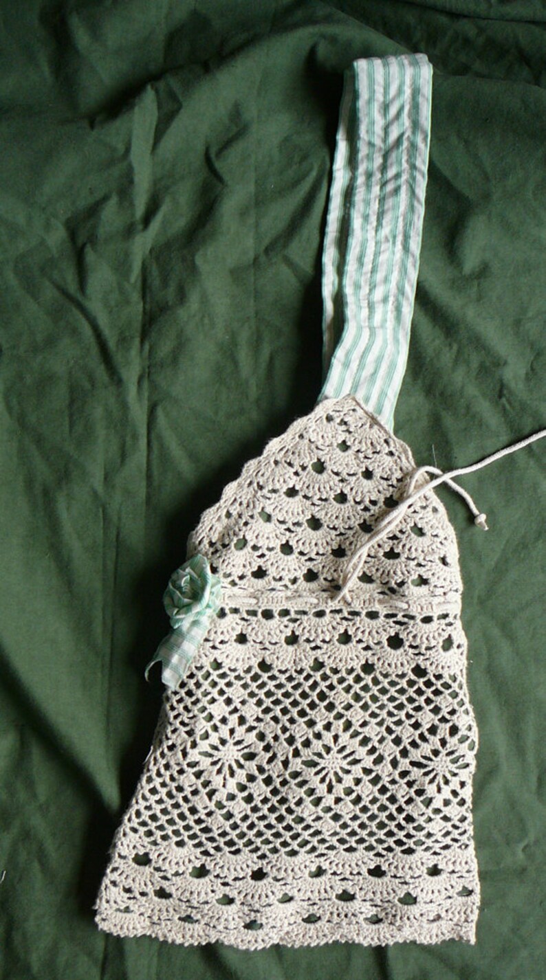 May include: A crocheted beige bag with a green and white striped fabric strap and a crocheted flower embellishment.