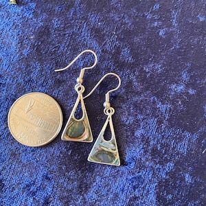 May include: A pair of silver earrings with a triangular shape and a green, blue, and brown abalone shell inlay. The earrings are hanging from a silver hook.