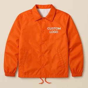 May include: Bright orange coach jacket with a white interior lining and a button-up front. The jacket features a collar, two front pockets, and a drawstring at the bottom hem. The text "CUSTOM LOGO" is printed on the chest.