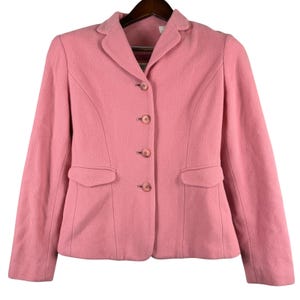 May include: A solid pink blazer featuring a notched lapel, long sleeves, and a four-button front closure. The jacket includes two front flap pockets and vertical seam detailing on the front panels, providing a structured fit with a classic collar.