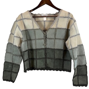 May include: A long-sleeve button-up jacket constructed from square suede patches in an ombre gradient from beige to dark sage green. The garment features a scalloped neckline and hem, with visible dark stitching connecting each square panel.