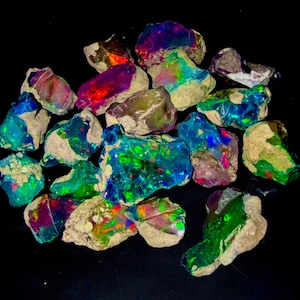May include: A collection of rough opal gemstones, showcasing vibrant colors including blues, greens, reds, and purples. The opals have a rough, natural texture with a mix of earthy tones and iridescent flashes.