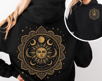 May include: Black hoodie featuring a gold celestial design on the back, including a sun, moons, and stars. The design is centered within a detailed circular pattern. A smaller version of the design is on the front. The hoodie has a drawstring hood.