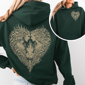 Può includere: Felpa con cappuccio verde scuro con un disegno a forma di cuore sul retro, raffigurante due figure ed elementi floreali beige. Il petto anteriore presenta un disegno più piccolo abbinato. La felpa ha una tasca a marsupio e un cappuccio.