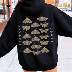 May include: Black hoodie featuring a gold moth and moon phase design on the back. The design includes multiple moths and a series of moon phases. The hoodie has a hood and a relaxed fit, suitable for casual wear.