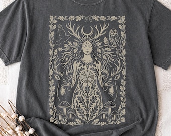 May include: A charcoal gray short-sleeve t-shirt featuring a cream-colored graphic print of a central figure with antlers, flanked by two deer, an owl, and a bird. The design includes a labyrinth symbol, mushrooms, and an oak leaf border frame.