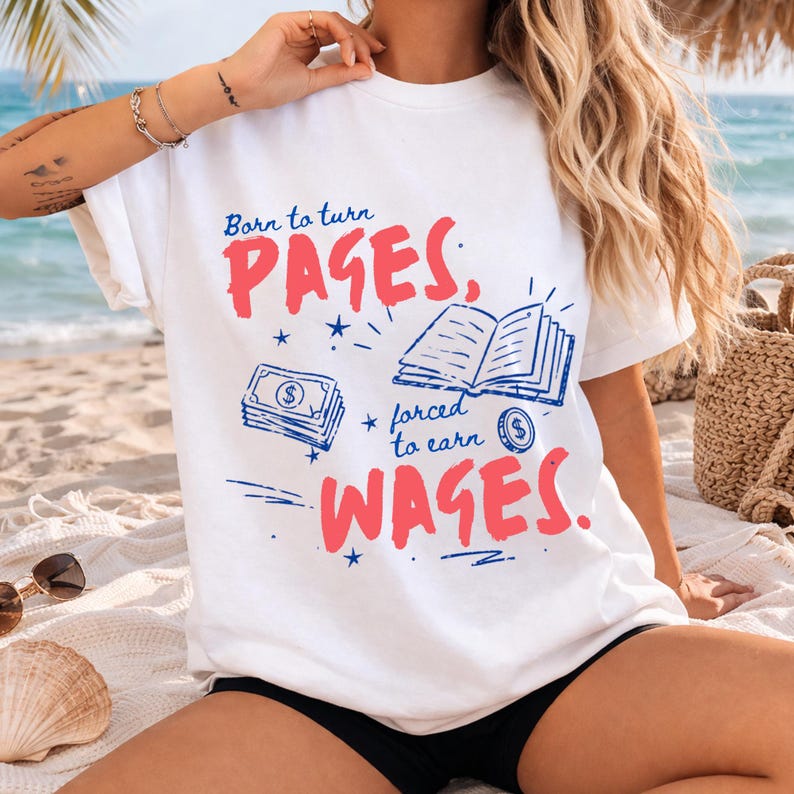 May include: White t-shirt with the text "Born to turn PAGES, forced to earn WAGES." The design includes illustrations of a stack of money, an open book, and a coin. The text and illustrations are in red and blue.