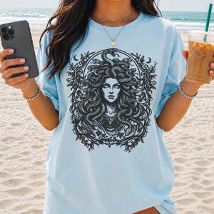 Op de afbeelding: Lichtblauw T-shirt met een zwart-wit afbeelding van Medusa, met slangen als haar, omringd door een bloemenkrans. Dit relaxte fit t-shirt is gemaakt van een zacht, comfortabel materiaal, perfect voor casual wear.