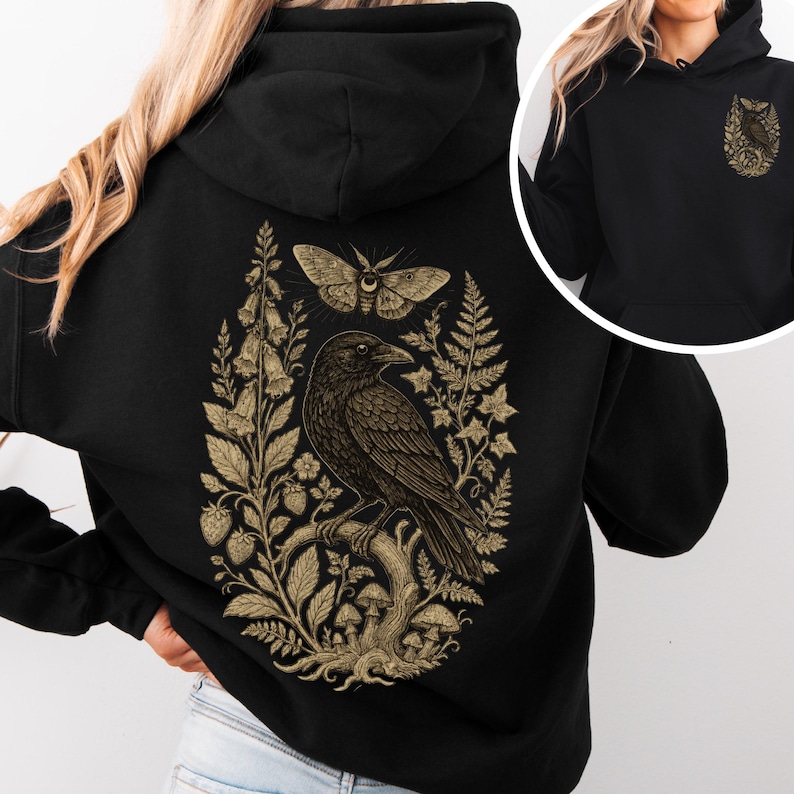 May include: A black hooded sweatshirt featuring a large gold-toned graphic on the back depicting a raven perched on a branch surrounded by mushrooms, ferns, foxgloves, strawberries, and a moth. A smaller version of the raven graphic is on the front.