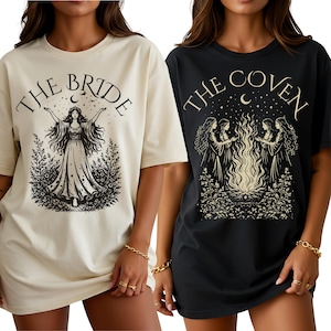Puede incluir: Dos camisetas holgadas, una crema y otra negra, con gráficos de brujas. La camiseta crema dice "THE BRIDE" con una ilustración de mujer. La camiseta negra dice "THE COVEN" con un grupo de mujeres alrededor de una hoguera.