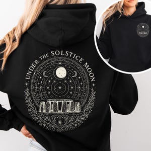 May include: Black hoodie featuring a circular design with the text "UNDER THE SOLSTICE MOON." The design includes a full moon, stars, crescent moons, and a depiction of Stonehenge. A smaller version of the design is on the front.