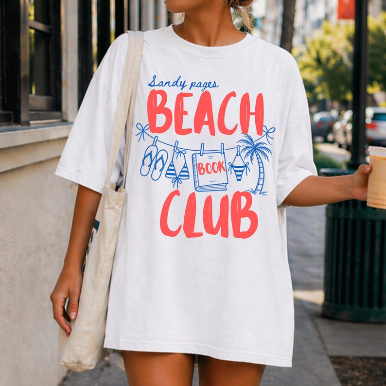 May include: White t-shirt with the text "Sandy pages BEACH CLUB" in red and blue. The design includes illustrations of flip-flops, a book, a bikini, and a palm tree, evoking a beach theme.