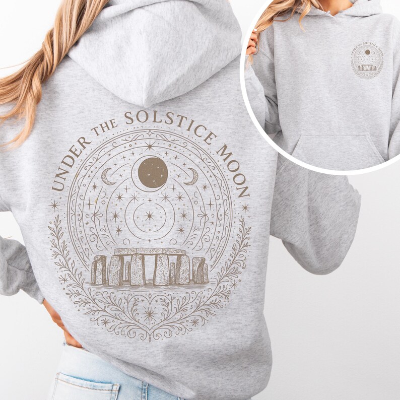 May include: Light gray hoodie with a drawstring hood and front pocket. The back features a circular graphic with the text "UNDER THE SOLSTICE MOON" surrounding an illustration of Stonehenge, a moon, stars, and crescent moons. A smaller version of the graphic is on the upper back.