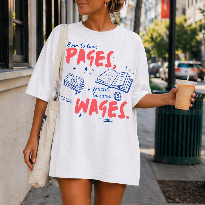 May include: White t-shirt with the text "Born to turn PAGES, forced to earn WAGES" in red and blue. The design includes illustrations of money and an open book. The shirt has short sleeves and a relaxed fit.