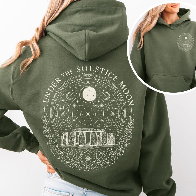May include: Olive green hoodie with a white graphic on the back featuring a circle design with the text "UNDER THE SOLSTICE MOON". The design includes a moon, stars, and Stonehenge. A smaller version of the design is on the front.