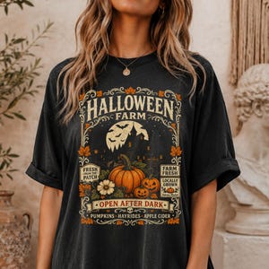 May include: A black t-shirt featuring a graphic print with the text HALLOWEEN FARM, FRESH FROM THE PATCH, FARM FRESH, LOCALLY GROWN, and OPEN AFTER DARK. The design includes a large pumpkin, smaller pumpkins, a full moon, bats, and autumn leaves.
