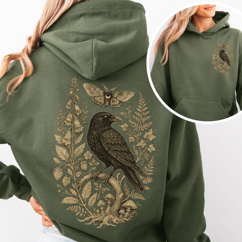 May include: An olive green hoodie with a detailed illustration of a raven perched on a branch, a moth, and botanical elements in brown and tan. A smaller version of the design is on the front pocket.