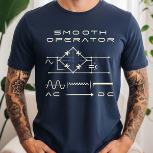 May include: Dark blue t-shirt featuring the text "SMOOTH OPERATOR" above a white electrical circuit diagram. Below the diagram are "AC" and "DC" with a graphic of an AC to DC converter.